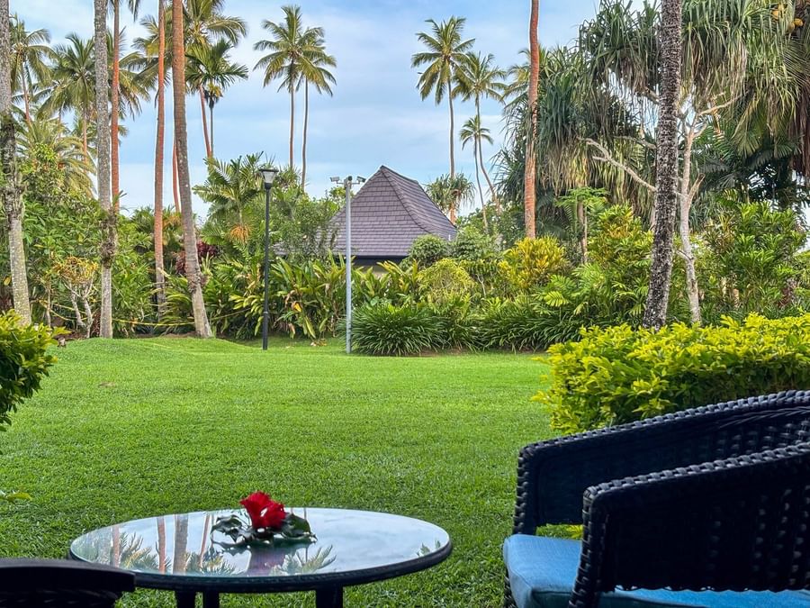 Two chairs and table with flower on grass by tropical trees and house at The Naviti Resort - Fiji.