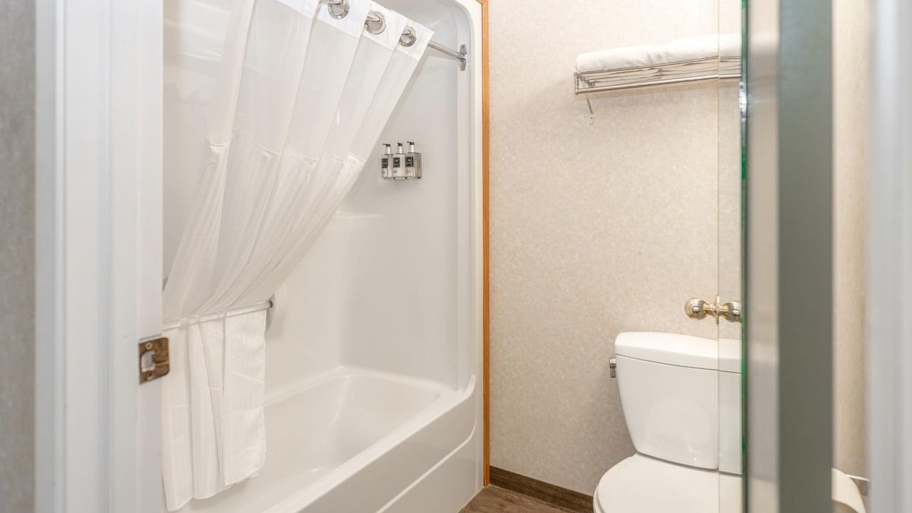 A bathroom with a toilet, shower with white curtain, and towel rack with folded towels.