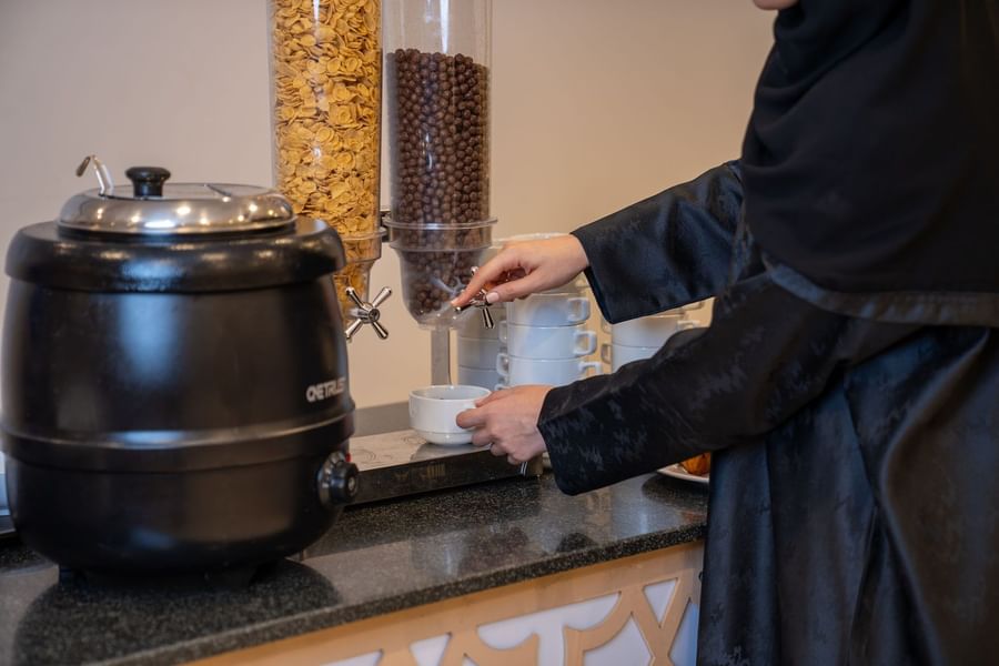 Guest using a cereal dispenser and coffee station in the breakfast buffet area at Saja by Warwick Makkah