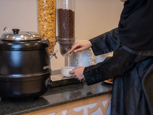 Woman dressed in black pouring hot beverage from a dispenser at Saja by Warwick Makkah.