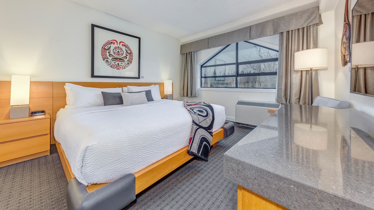 Hotel room with a large bed, nightstands, framed artwork, and a window with curtains.