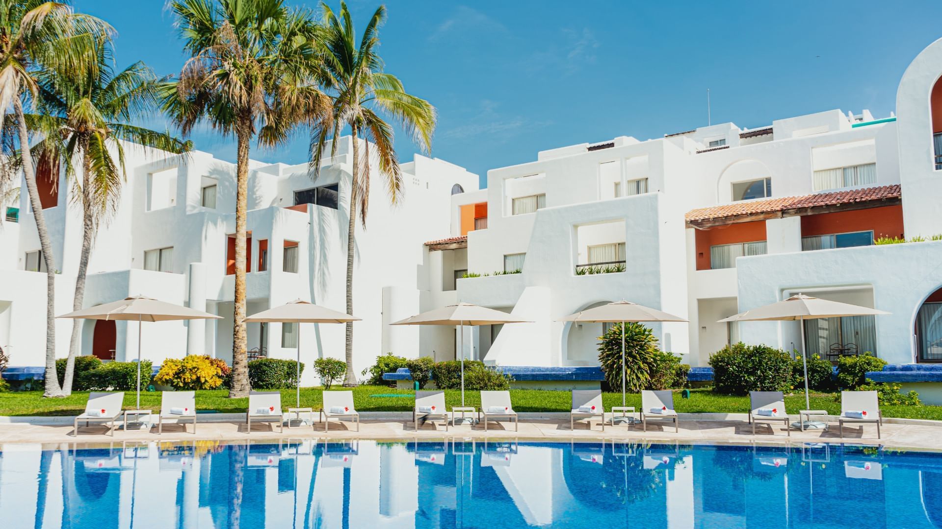Tropical white villas and loungers by the sparkling blue swimming pool at Camino Real Zaashila Huatulco