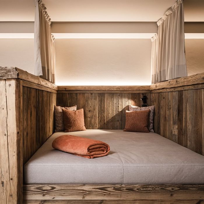 Wooden bunk bed with pillows and blanket, enclosed by wooden walls and curtains for privacy.