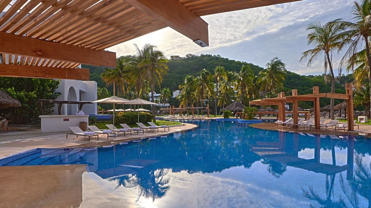 Poolside area at Camino Real Zaashila Huatulco, with grey loungers under a modern wooden pergola