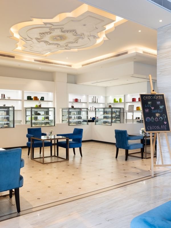 Chocolate Café featuring blue chairs by white shelving units and a chalkboard easel at Warwick Al Khobar