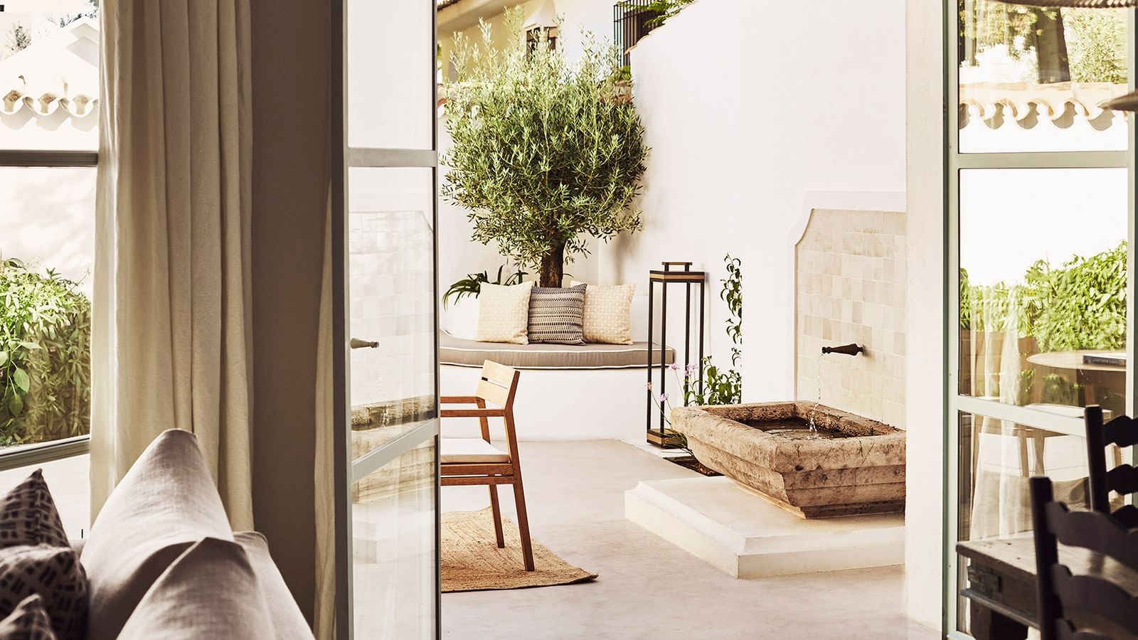 Chiquita private patio with an olive tree, built-in cushioned seating, & a stone water fountain at Marbella Club