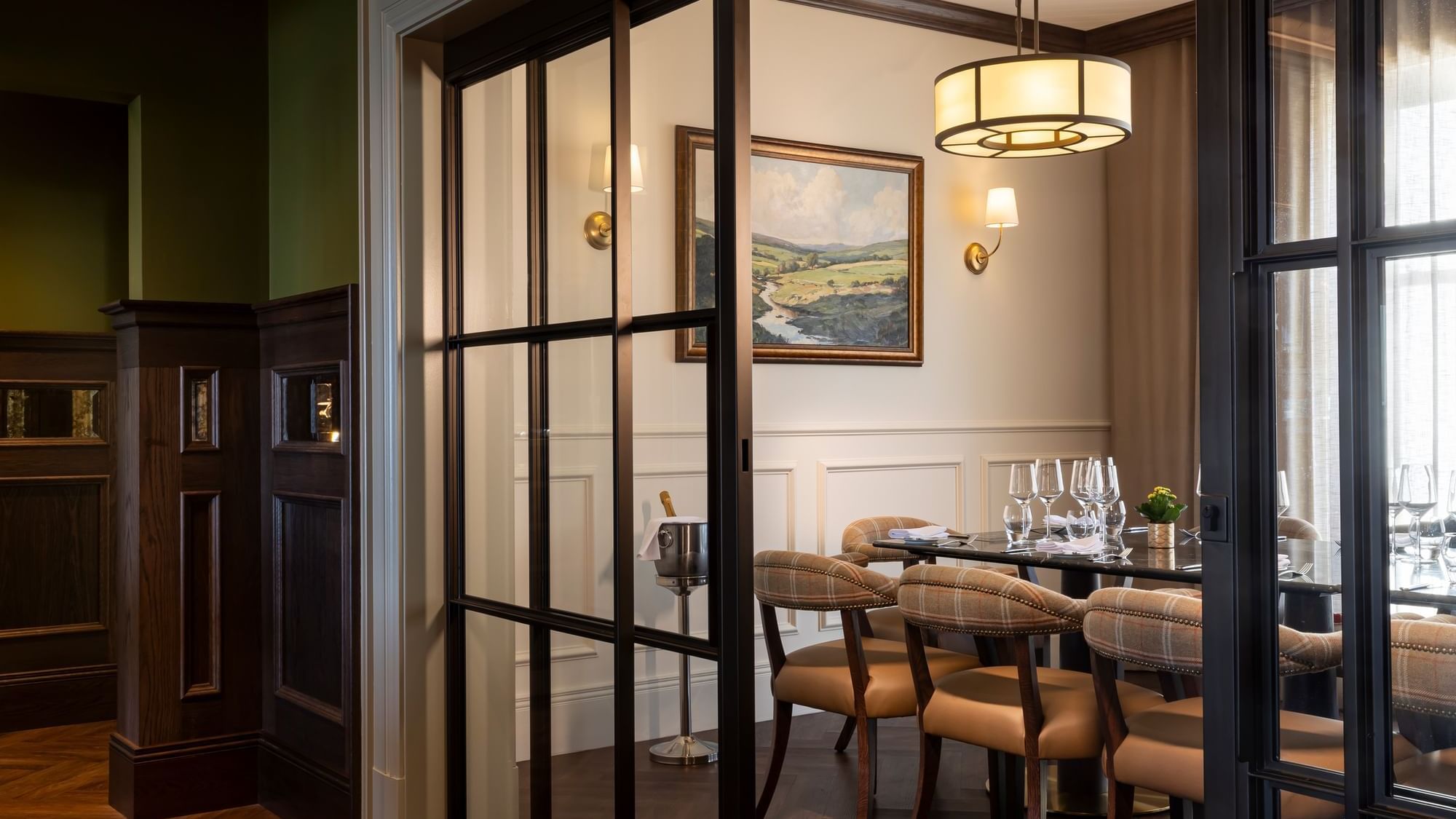 Private dining area with a round table, plaid chairs, and a painting on the wall, separated by glass doors at Dunluce Lodge