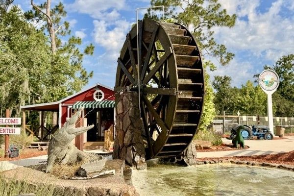A large wooden mill wheel beside an alligator fountain at the entrance to The Showcase of Citrus in Clermont.
