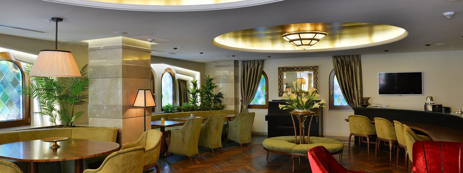 Green armchairs on a herringbone floor by a table under a gold ceiling near lamps in Lobby Lounge at Warwick Ankara