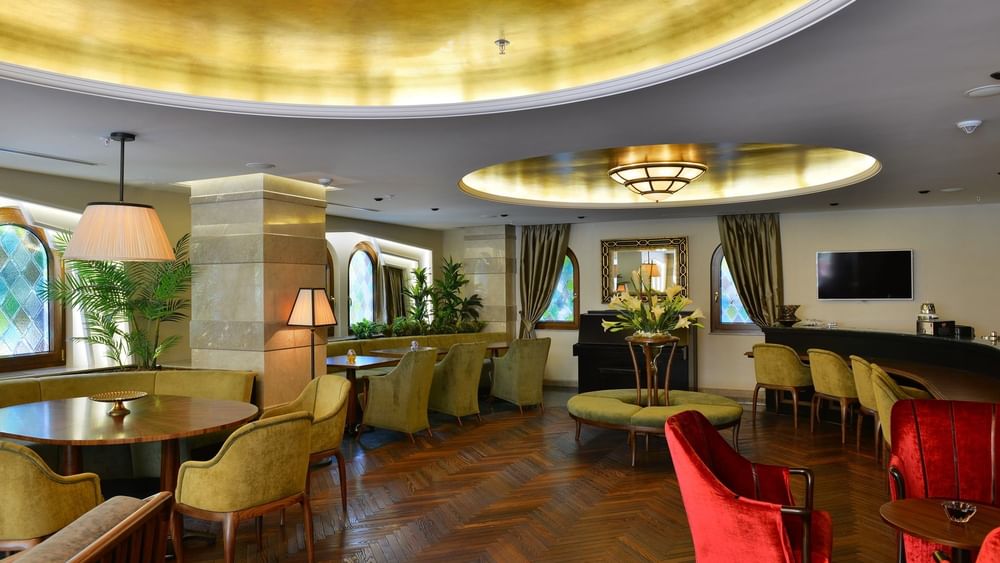 Green armchairs on a herringbone floor by a table under a gold ceiling near lamps in Lobby Lounge at Warwick Ankara
