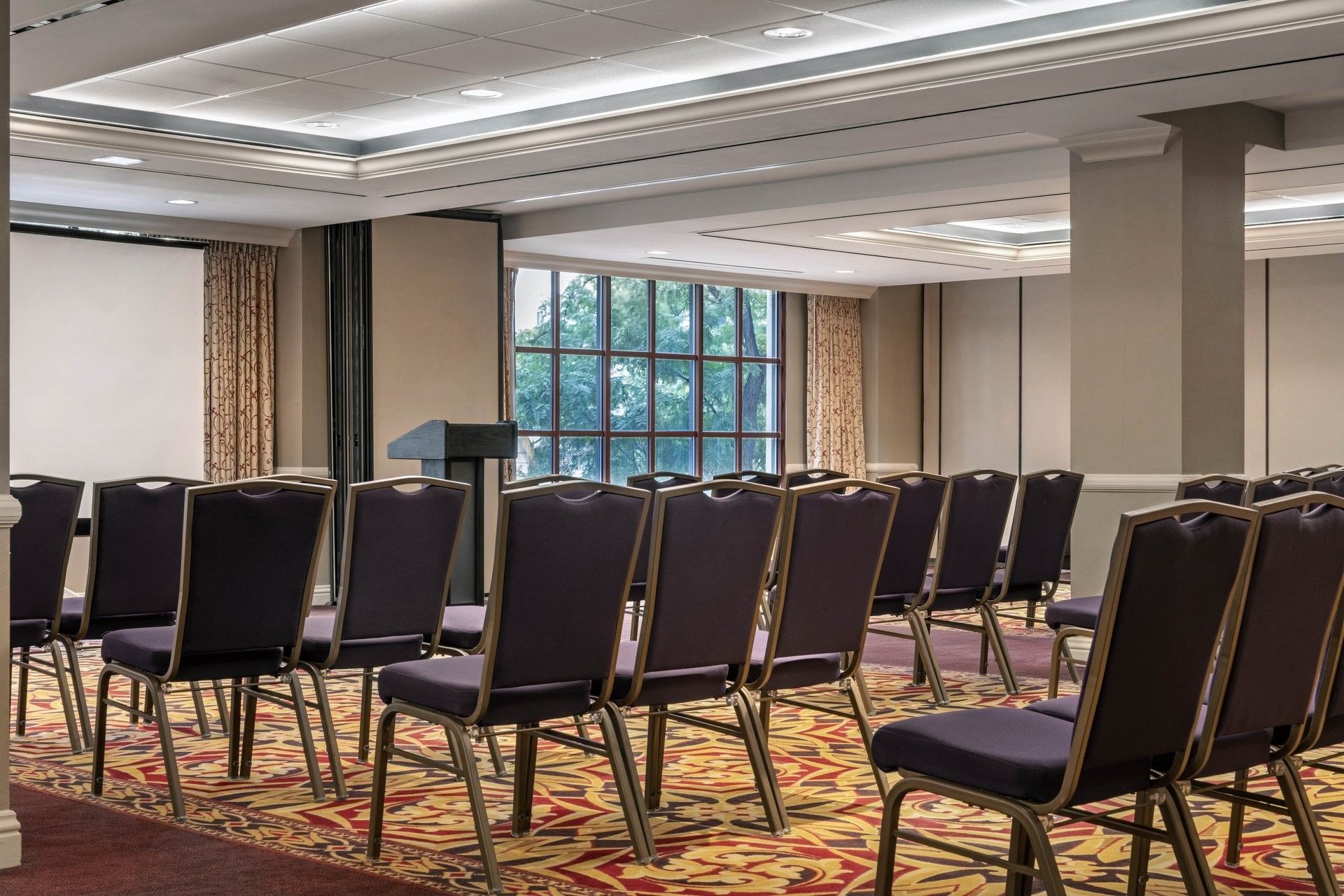 Rows of purple chairs by a podium under a bright ceiling in Capitol Ballroom at Warwick Denver