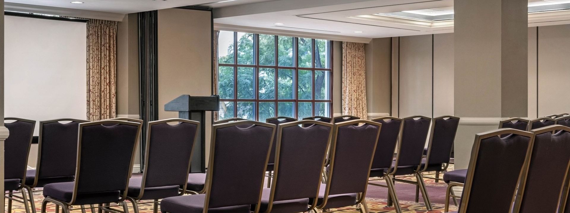Rows of purple chairs by a podium under a bright ceiling in Capitol Ballroom at Warwick Denver
