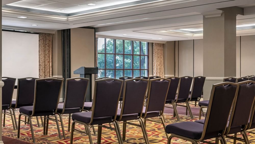 Rows of purple chairs by a podium under a bright ceiling in Capitol Ballroom at Warwick Denver