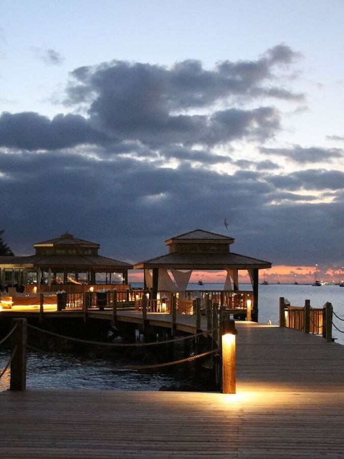 Wooden pier by gazebos under a twilight sky surrounding calm harbor water at Warwick Paradise Island Bahamas
