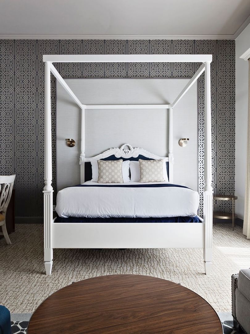 Four-poster bed by a desk and grey sofa under a patterned wall in Balcony Junior Suite at Warwick San Francisco