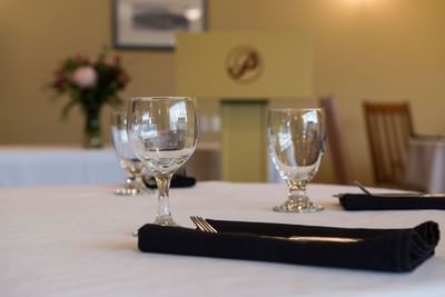 Forks wrapped in a black napkin with two wine glasses on a white tablecloth in The Okanagan at Hilltop Inn Salmon Arm