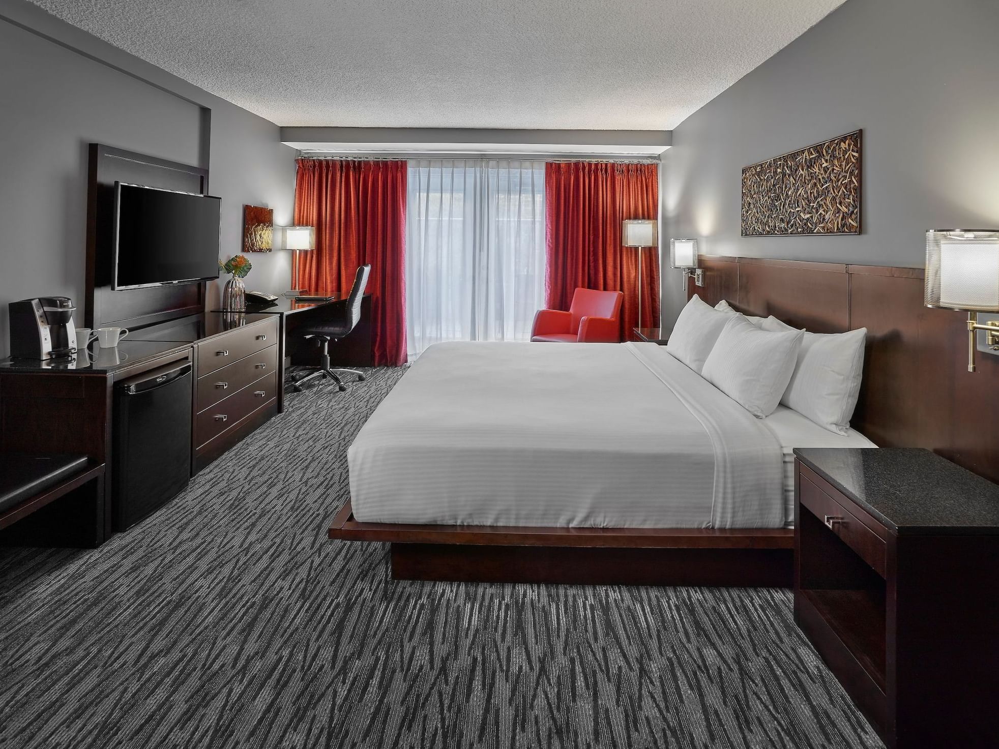 A hotel room with a large bed, desk, red chairs, and a window with curtains.