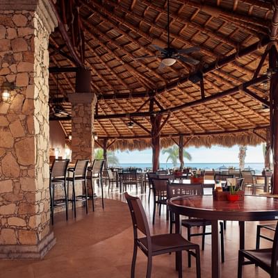 Sirenas restaurant with stone pillars, a thatched roof, and ocean views at Hacienda del Mar Los Cabos.