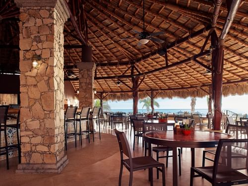 Sirenas restaurant with stone pillars, a thatched roof, and ocean views at Hacienda del Mar Los Cabos.