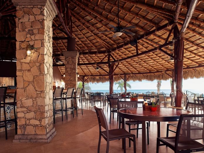 Sirenas restaurant with stone pillars, a thatched roof, and ocean views at Hacienda del Mar Los Cabos.