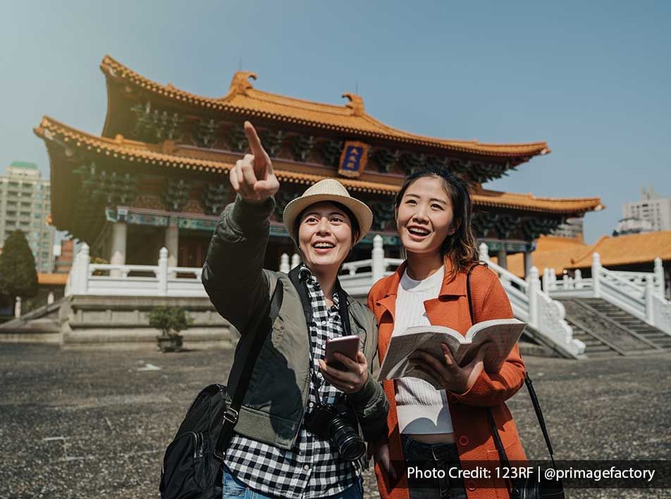 Two female tourists sightseeing near a chinese temple with a guidebook - Lexis Port Dickson