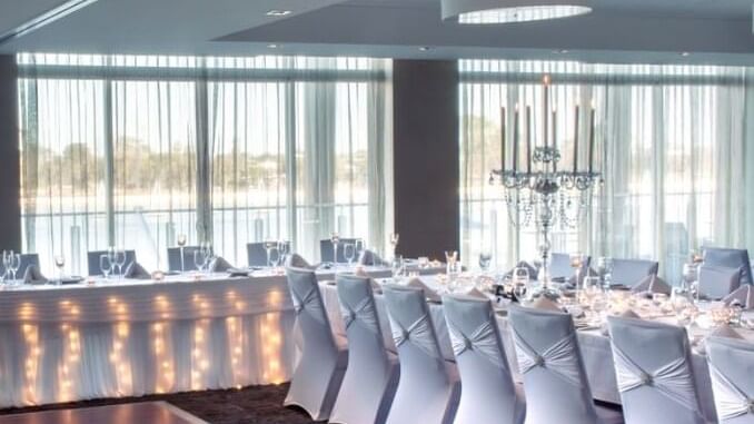 Wedding reception with long tables covered with white tablecloths and illuminated lights at The Sebel Mandurah