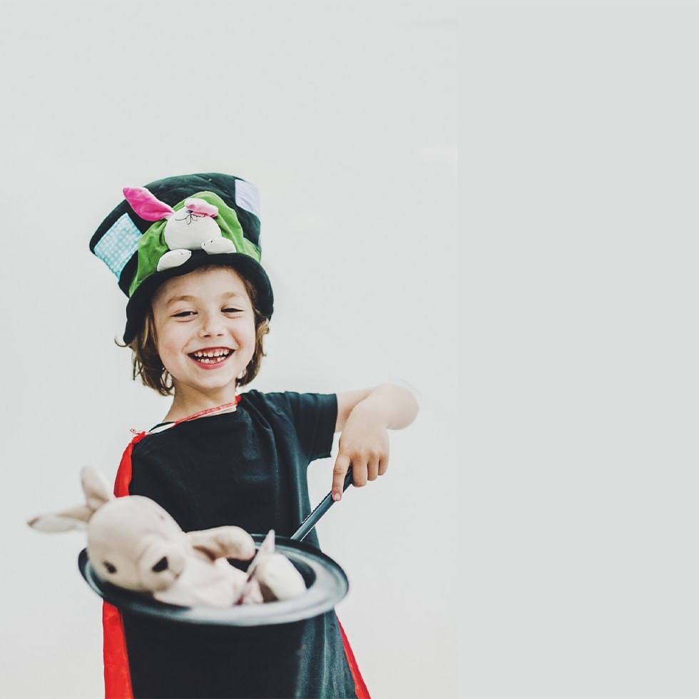 Bambino vestito da mago sorridente con un cappello e un coniglio nel cappello magico.