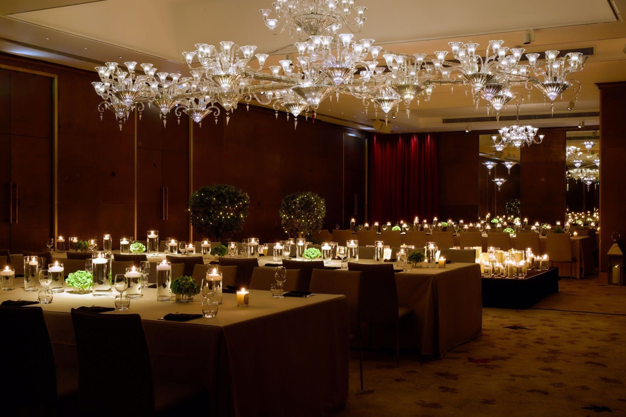 Chandeliers above a dining room with tables and chairs set for private dinner at The Crystal Ballroom at The May Fair Hotel, London.