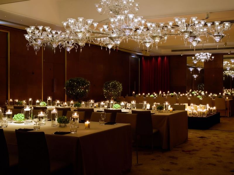 Chandeliers above a dining room with tables and chairs set for private dinner at The Crystal Ballroom at The May Fair Hotel, London.