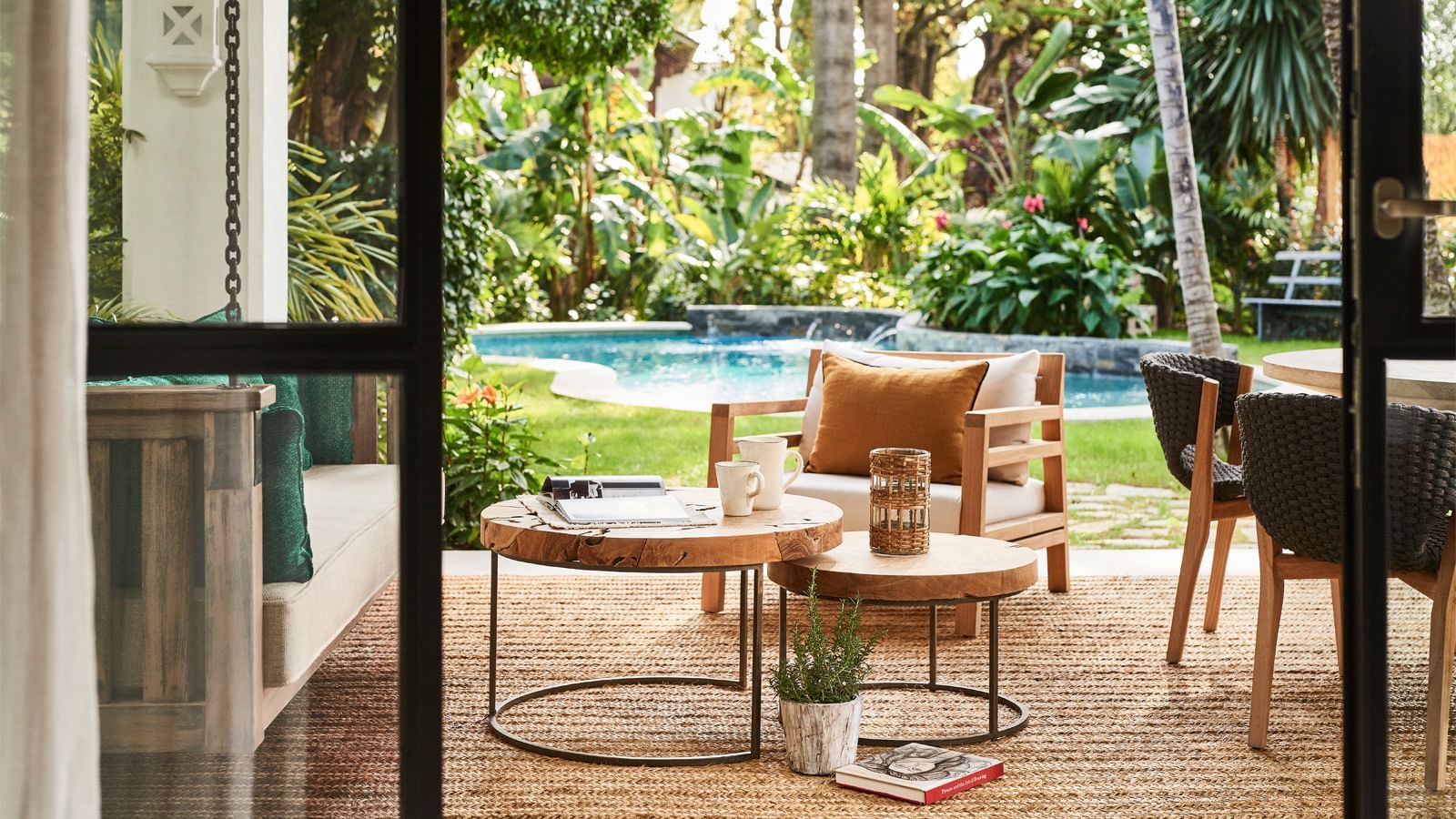 Outdoor sitting area with wood nesting tables placed on a woven rug by a pool at the Marbella Club