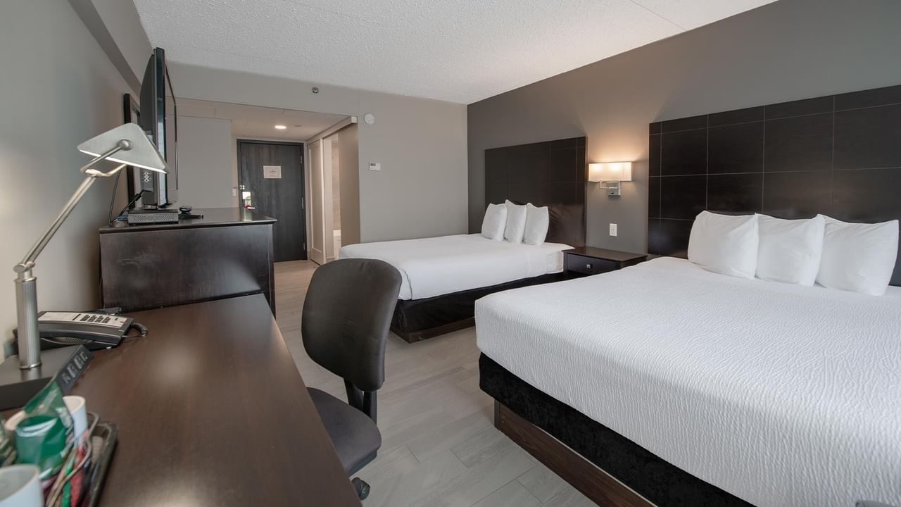 Hotel room with two queen beds, a desk with a lamp, and a chair.