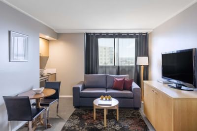 Dining table, sofa & TV in a room at Nesuto Hotels