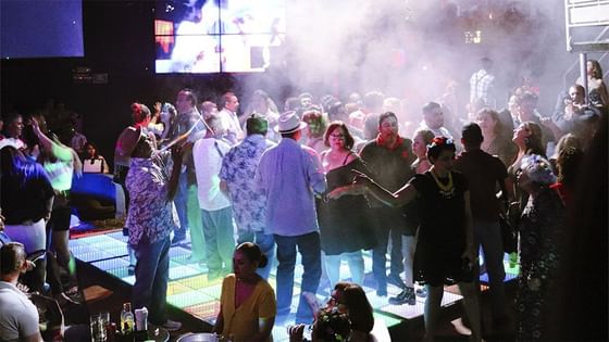 Multitud de personas bailando sobre pista iluminada con niebla ambiental en El Rollo de Araiza Palmira