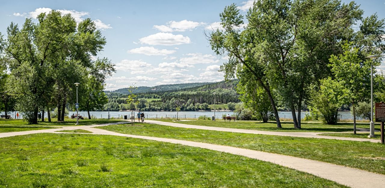 Concrete walkways weaving through green grass lawns by a wide open riverbank view near Coast Whitecourt Hotel