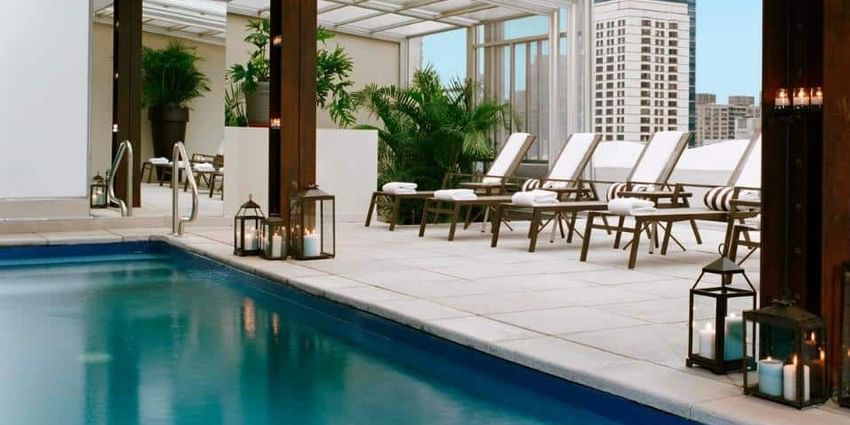 A rooftop pool with lounge chairs, lanterns, and plants
