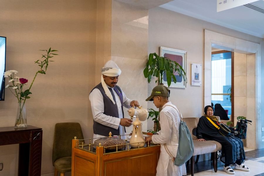 Hotel staff in traditional attire serving Arabic coffee to a guest in a luxury lobby at Saja by Warwick Makkah