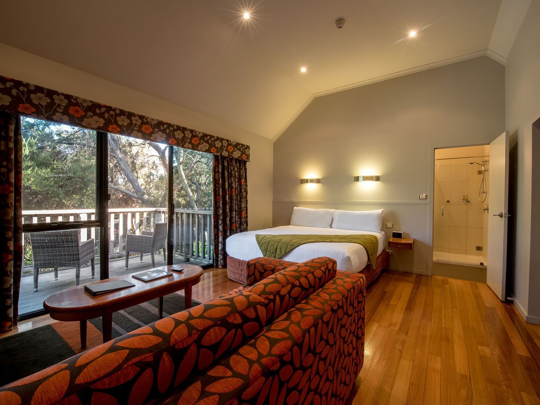 Sofa by the bed in One Room Cabin bedroom with wooden floors at Freycinet Lodge