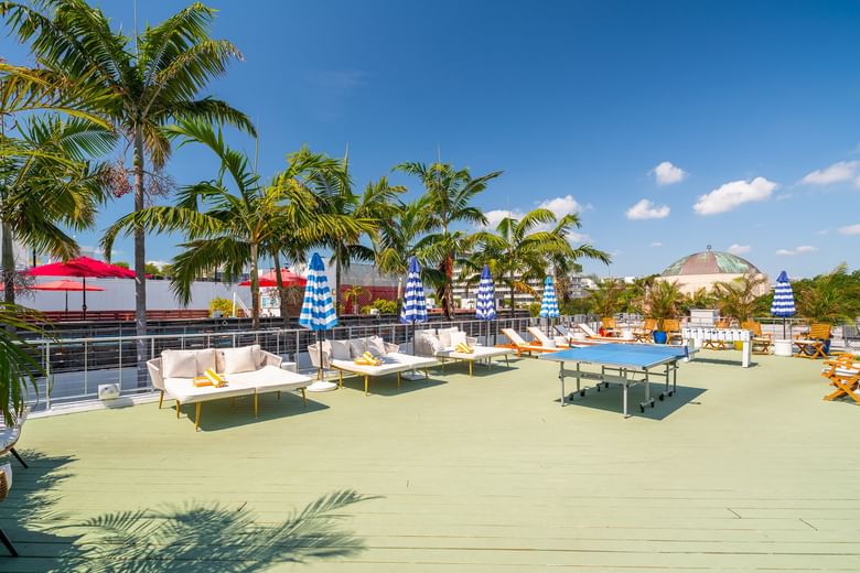 A poolside area with outdoor furniture, palm trees, and a ping pong table.