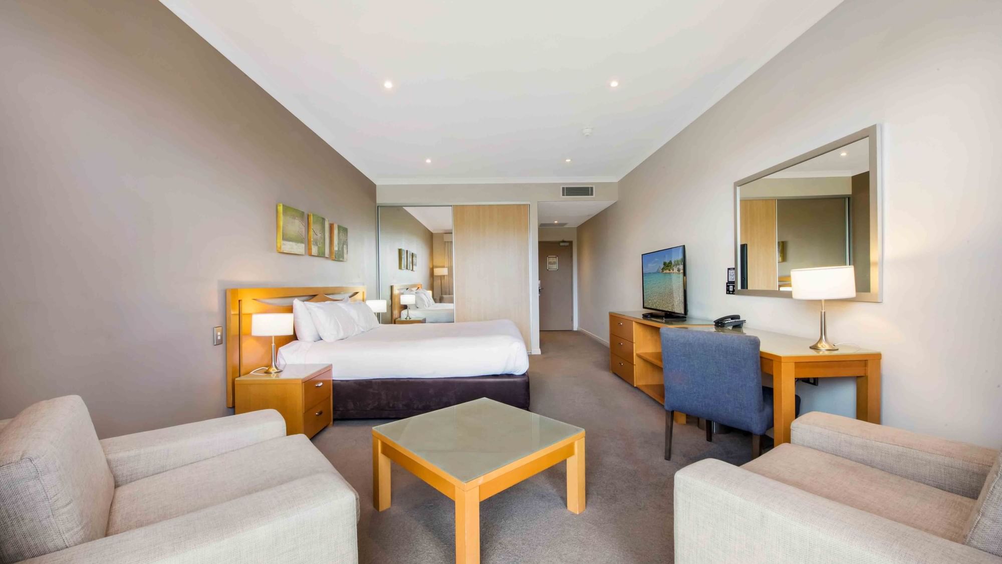 Deluxe Golf View Room with a large bed, sitting area, desk, TV, and reflective wall mirror at Mercure Kooindah Waters