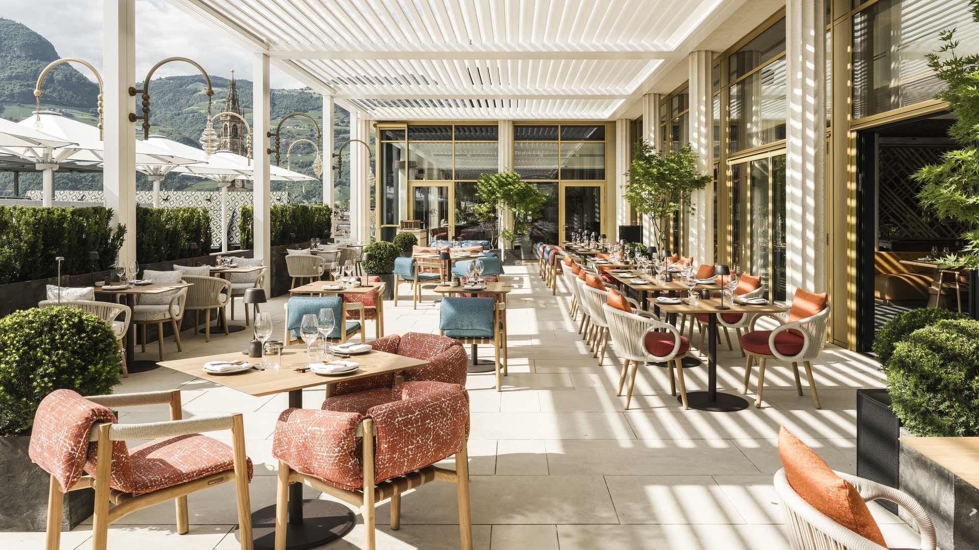 Ristorante esterno con tavoli e sedie, piante e vista sulle montagne.