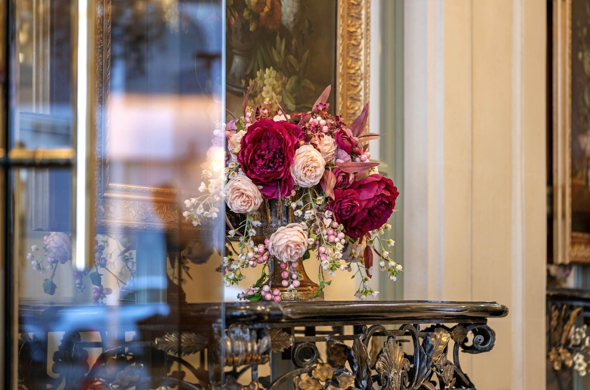 Lush bouquet of deep red and pink flowers placed in a golden vase by a vintage ornate table at Hotel Westminster Paris