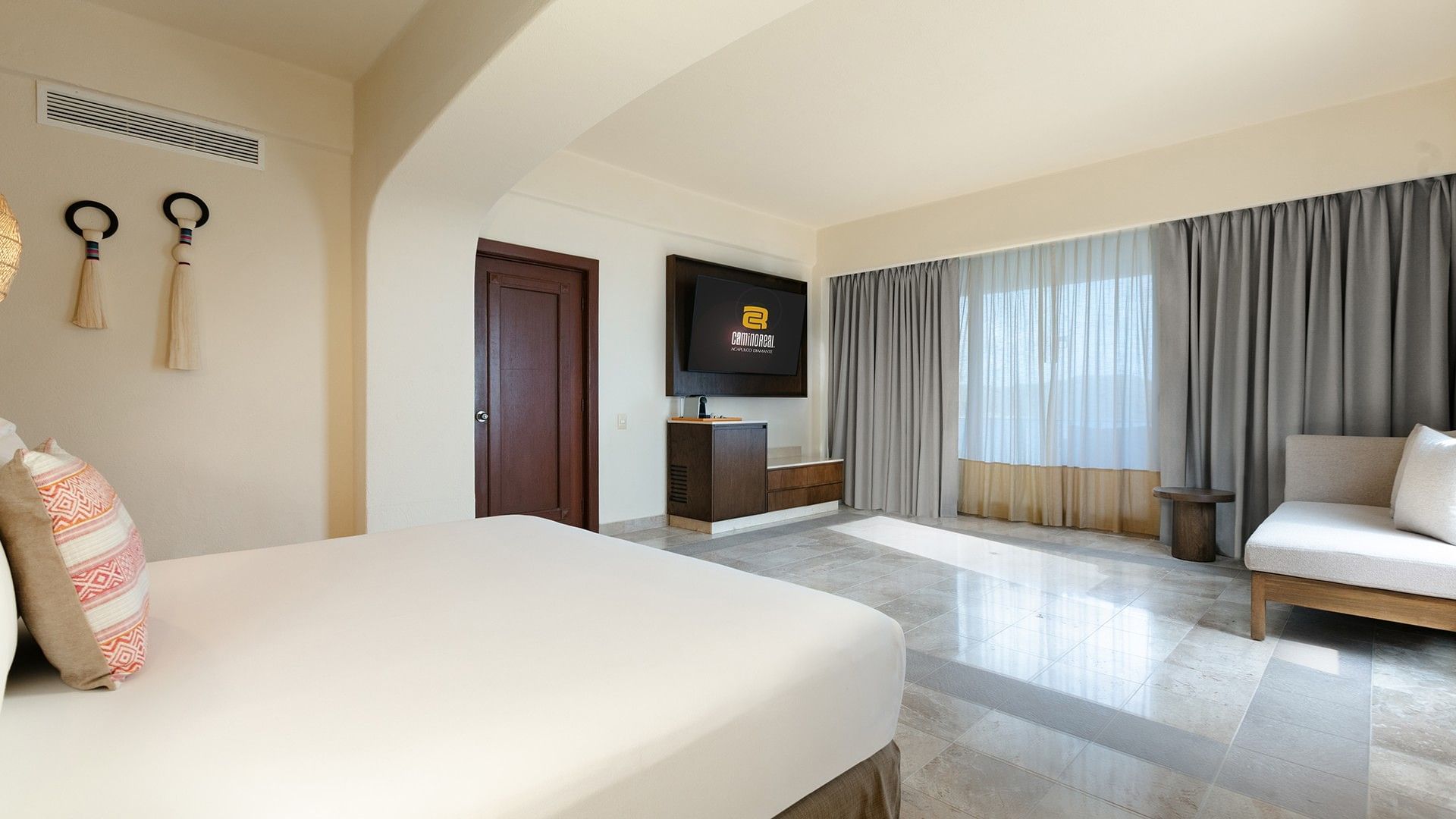 King Master Suite with a white bed, marble floors, and a TV mounted on a dark wood wall at Camino Real Acapulco Diamante