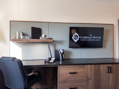 A desk with coffee maker, phone, and flat screen TV from Carriage House Hotel & Conference Centre