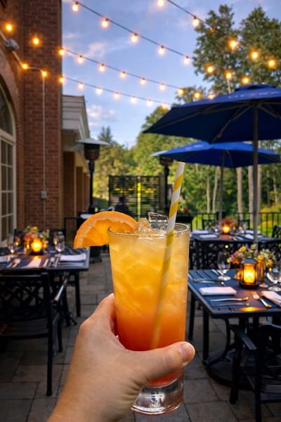 Iced orange cocktail with a yellow striped straw on a patio table during Sunset Summer Dining at Avon Old Farms Hotel