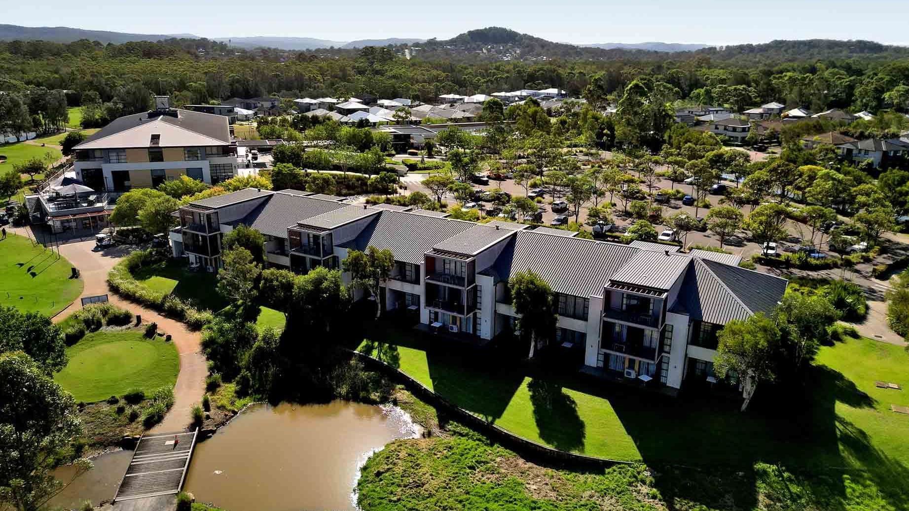 Aerial view of Mercure Kooindah Waters with a pond, and a parking lot surrounded by greenery