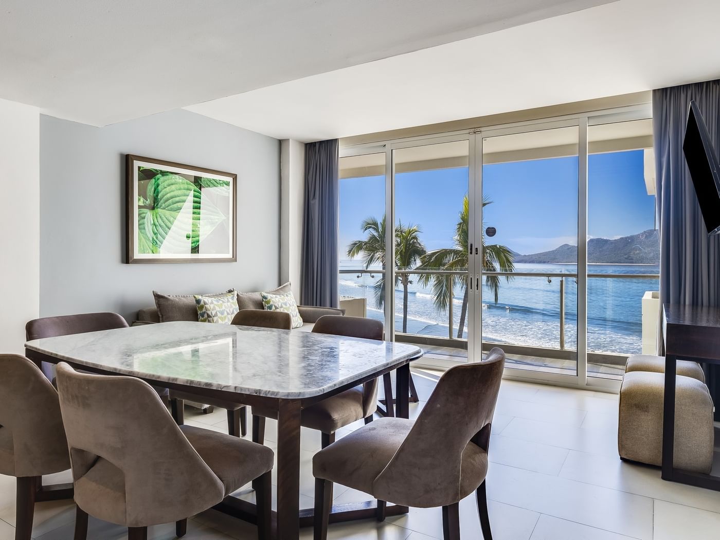 Luxury Suite dining area with a marble table and a stunning ocean view through glass at Sunvivia Mazatlán