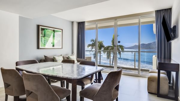Luxury Suite dining area with a marble table and a stunning ocean view through glass at Sunvivia Mazatlán