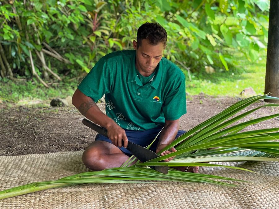 Man with a green polo shirt cutting a palm leaf with a knife at The Naviti Resort.