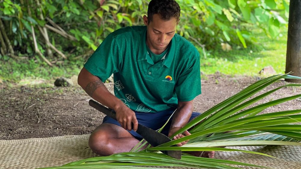 Man weaving palm leaves with a machete at The Naviti Resort in Korolevu.