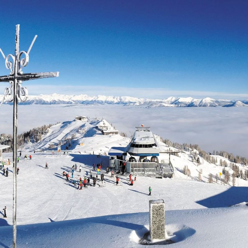 Skifahrer und Snowboarder auf einem verschneiten Berghang, umgeben von einer Nebelschicht und fernen Bergen.